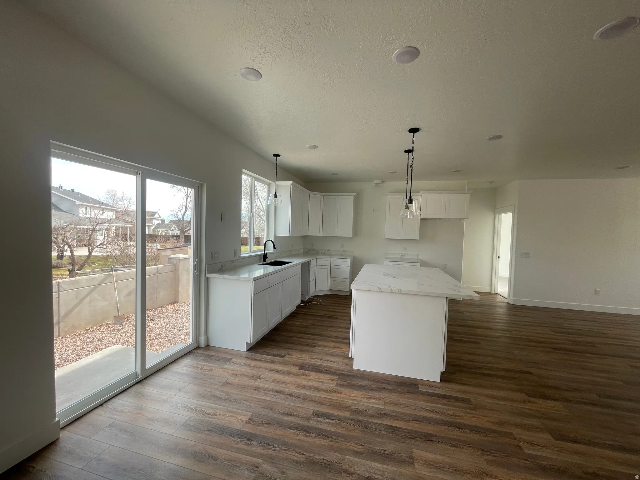 Kitchen featuring a kitchen island, white cabinetry, dark wood finished floors, light stone countertops, and hanging light fixtures