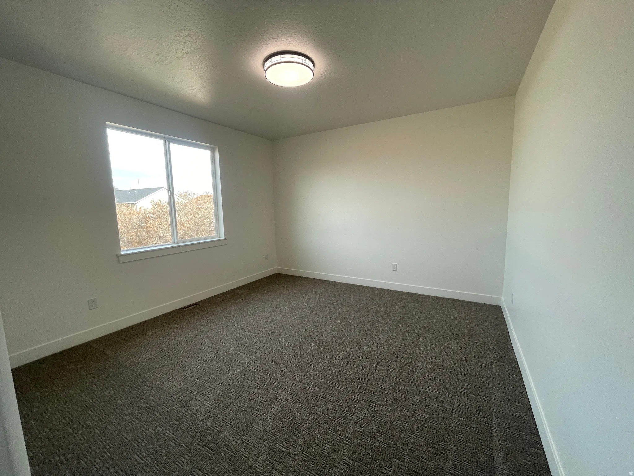 Empty room featuring dark colored carpet and a textured ceiling