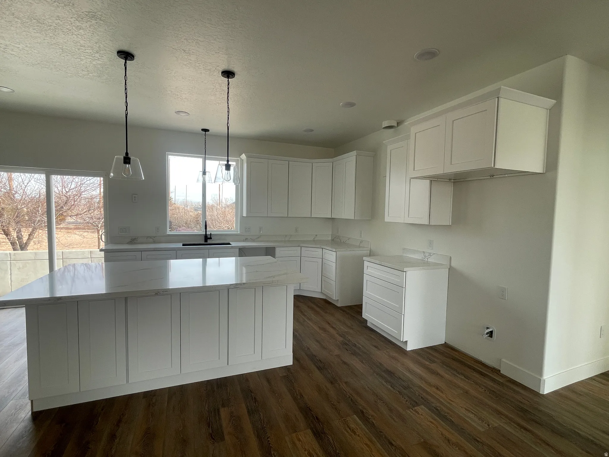 Kitchen featuring white cabinetry, hanging light fixtures, dark wood finished floors, light stone counters, and a kitchen island