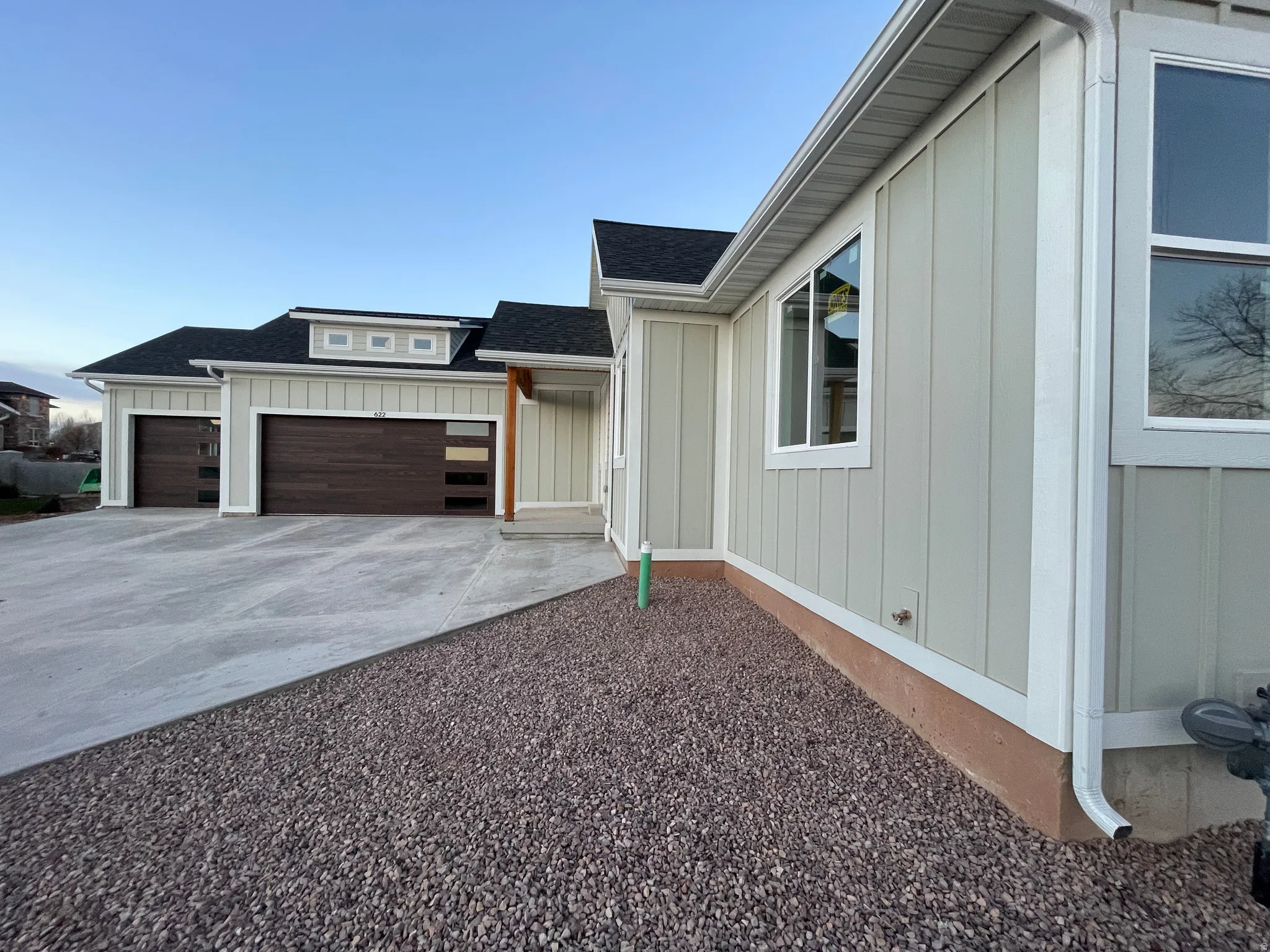 Property entrance with board and batten siding, driveway, an attached garage, and a shingled roof