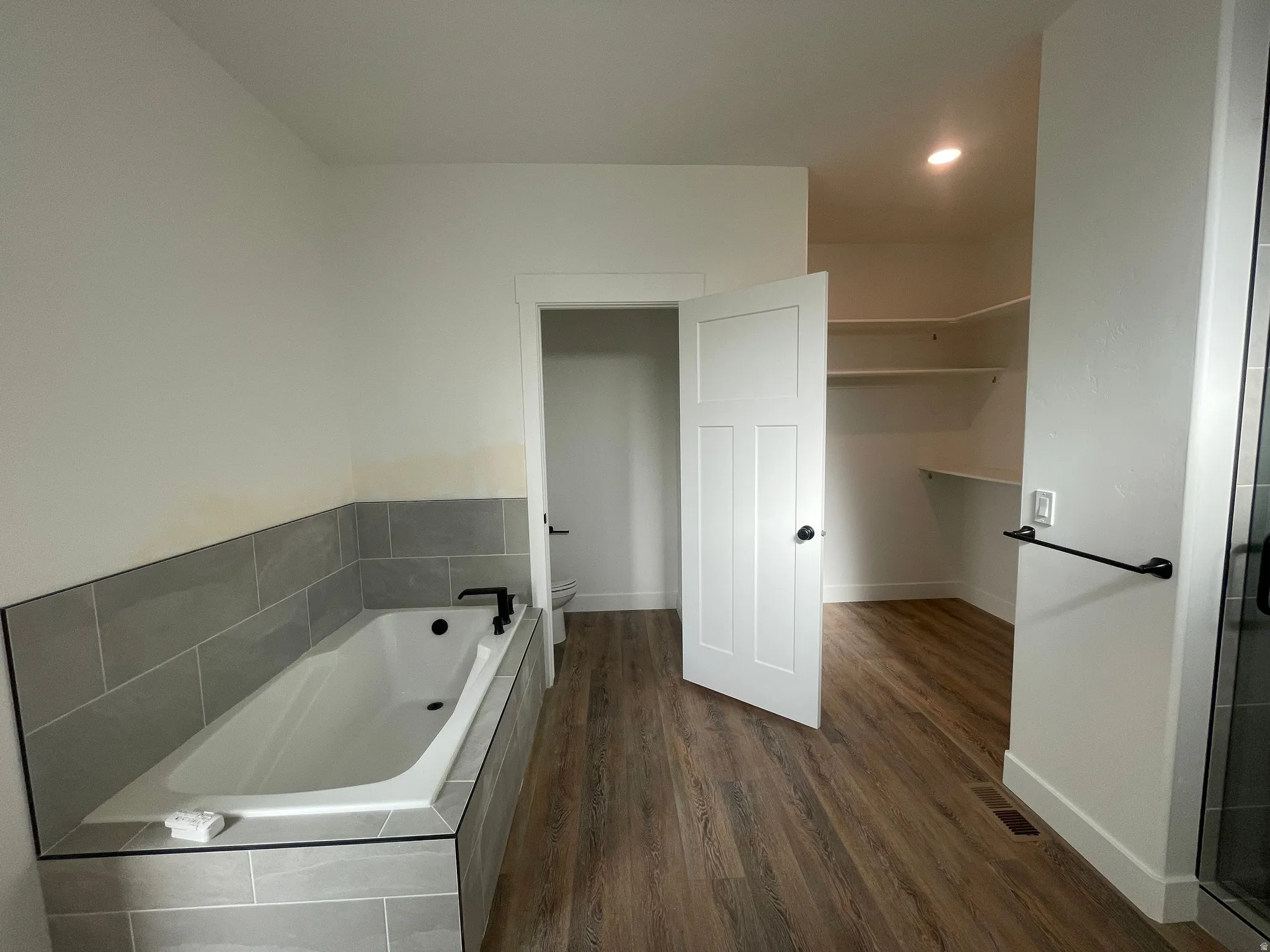 Bathroom featuring dark wood-style flooring, a garden tub, a walk in closet, and recessed lighting