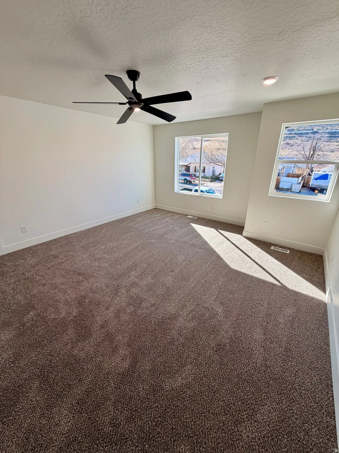 Carpeted empty room featuring a textured ceiling and a ceiling fan