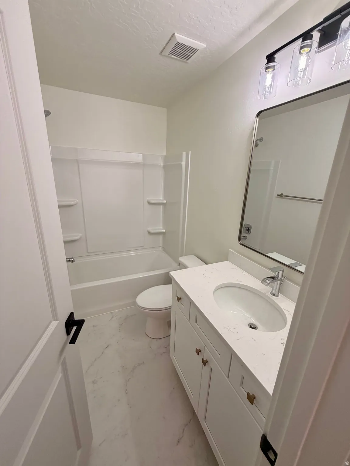 Full bath featuring vanity, light marble finish flooring, tub / shower combination, and a textured ceiling