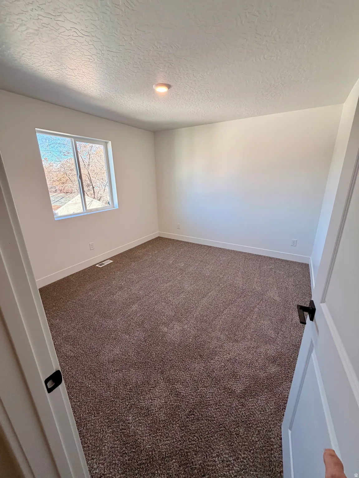 Empty room with dark colored carpet and a textured ceiling