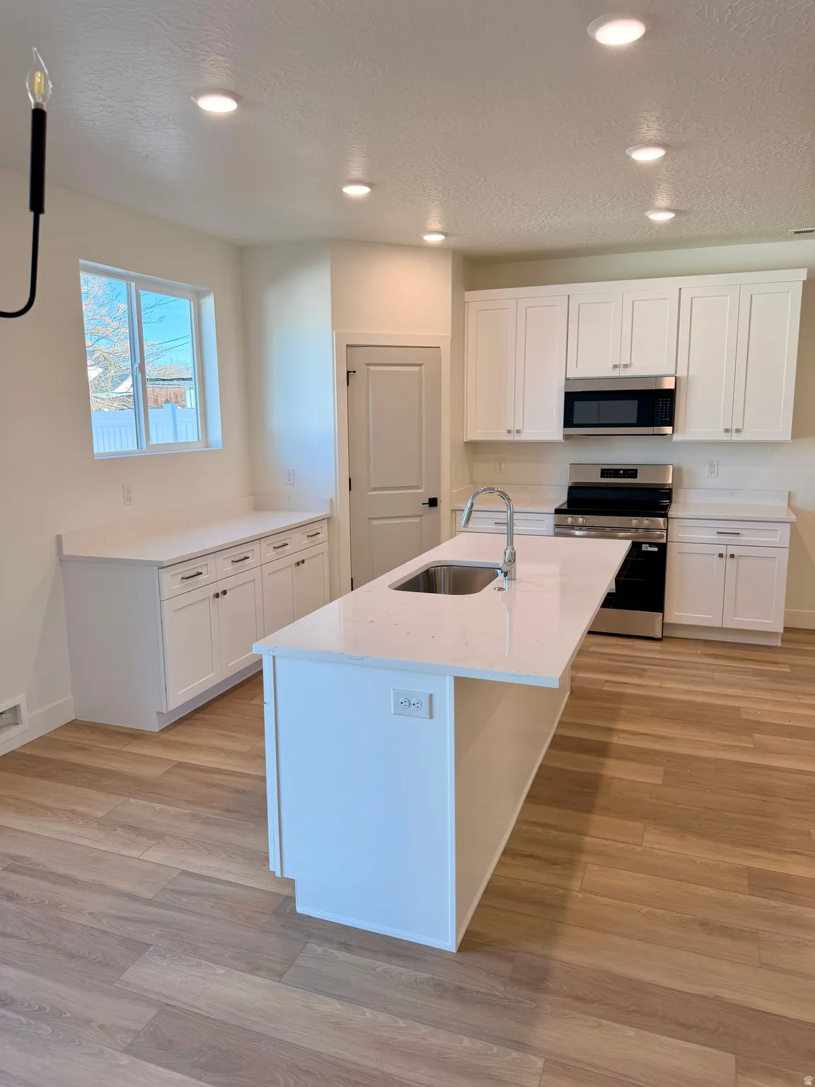 Kitchen with white cabinets, stainless steel appliances, light stone countertops, a kitchen island with sink, and recessed lighting