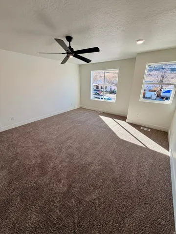 Carpeted empty room featuring a textured ceiling and a ceiling fan