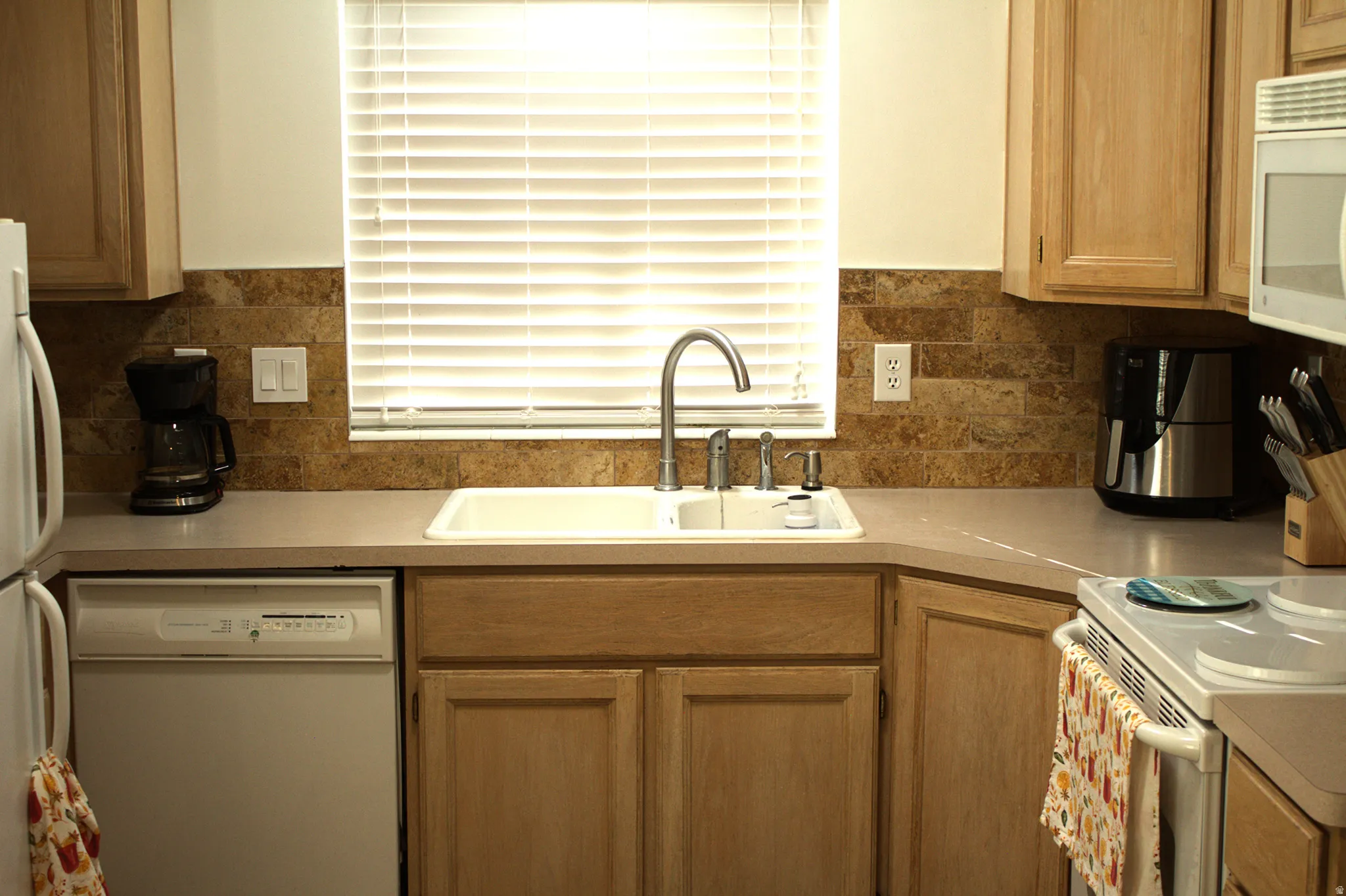 Kitchen with white appliances, light countertops, decorative backsplash, and brown cabinets