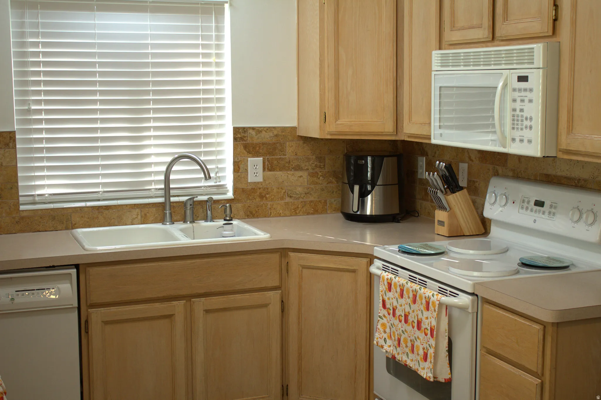 Kitchen featuring white appliances, light brown cabinetry, light countertops, and tasteful backsplash