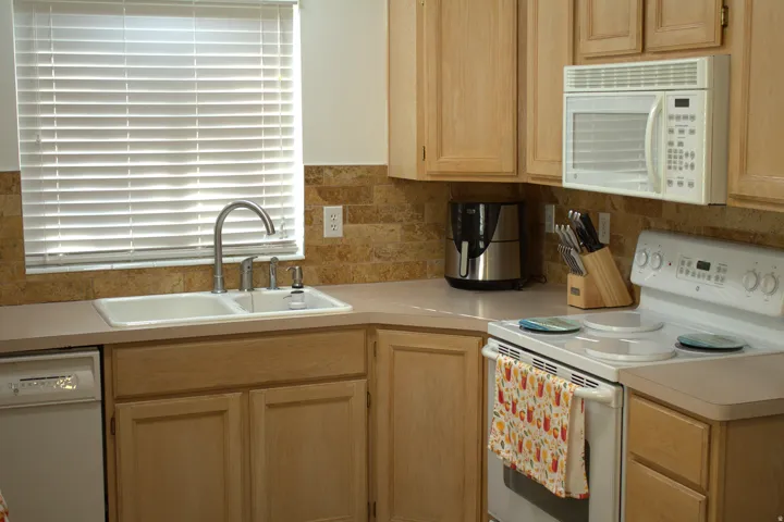 Kitchen featuring white appliances, light brown cabinetry, light countertops, and tasteful backsplash