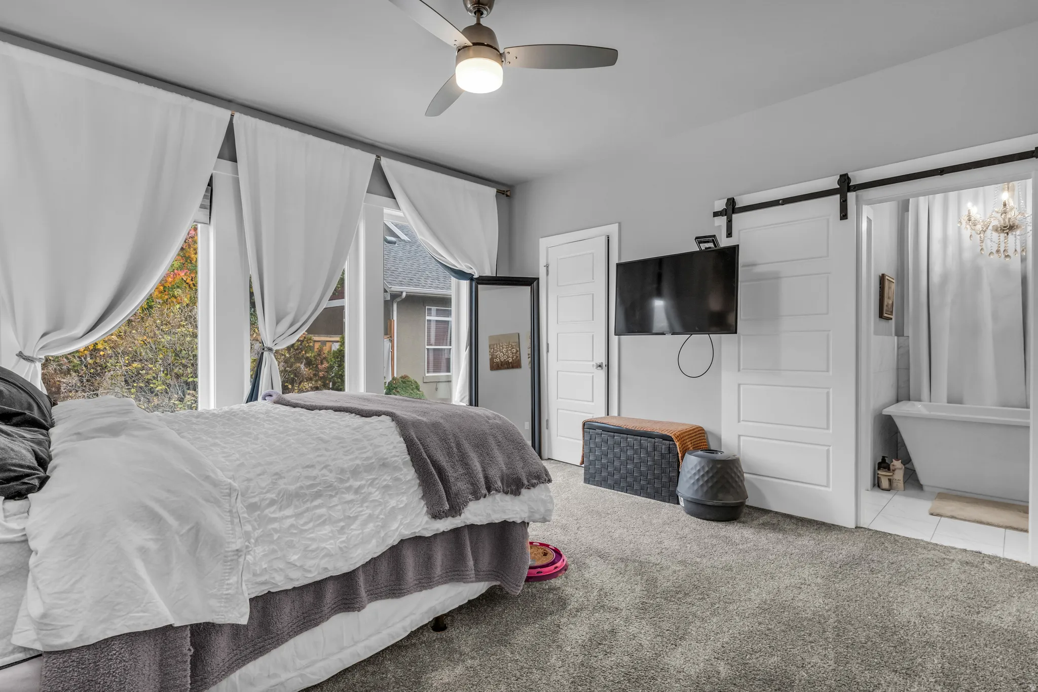 Bedroom with a barn door, carpet floors, a ceiling fan, connected bathroom, and tile patterned floors