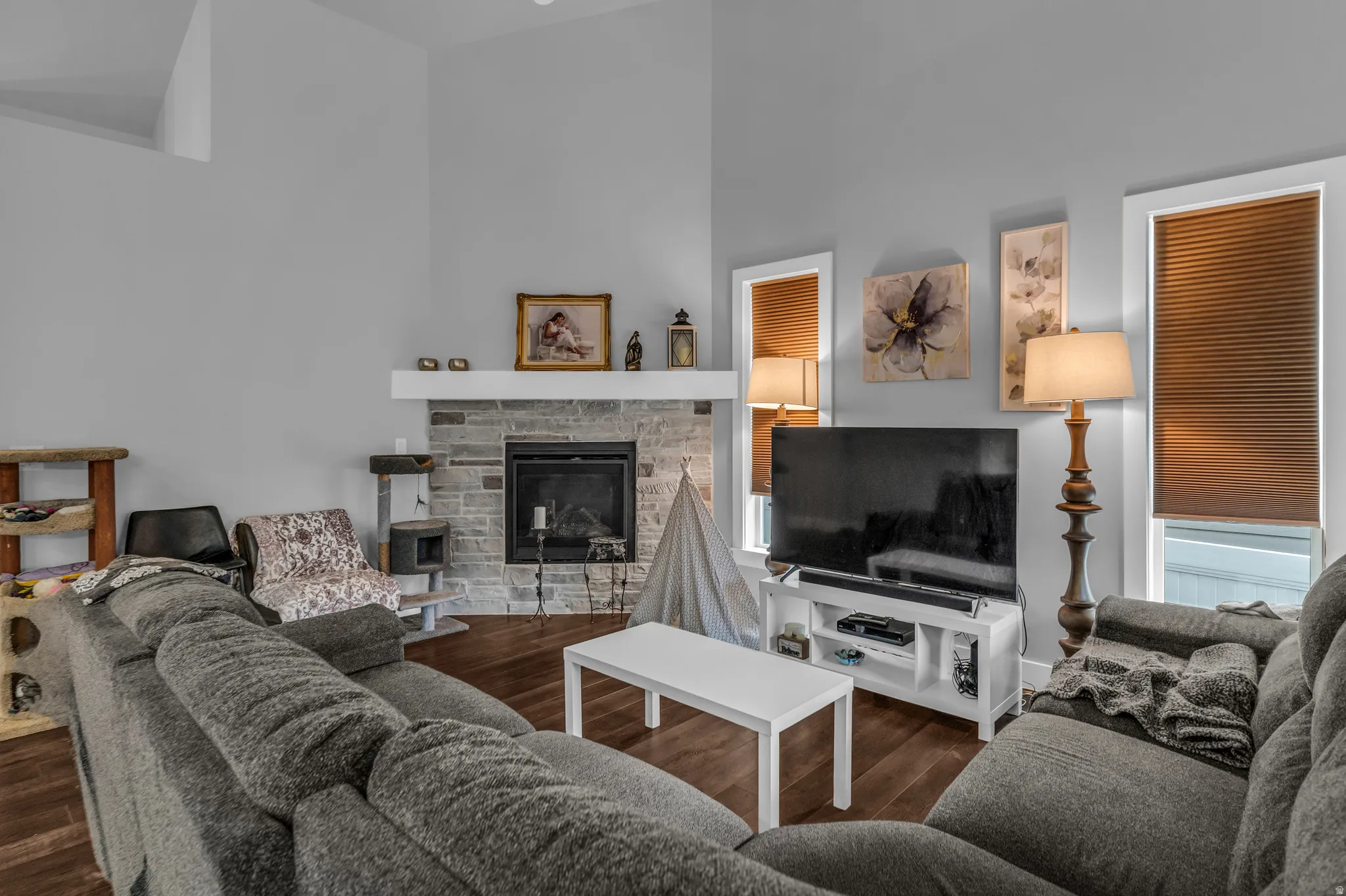 Living room featuring a towering ceiling, dark wood-style floors, and a stone fireplace