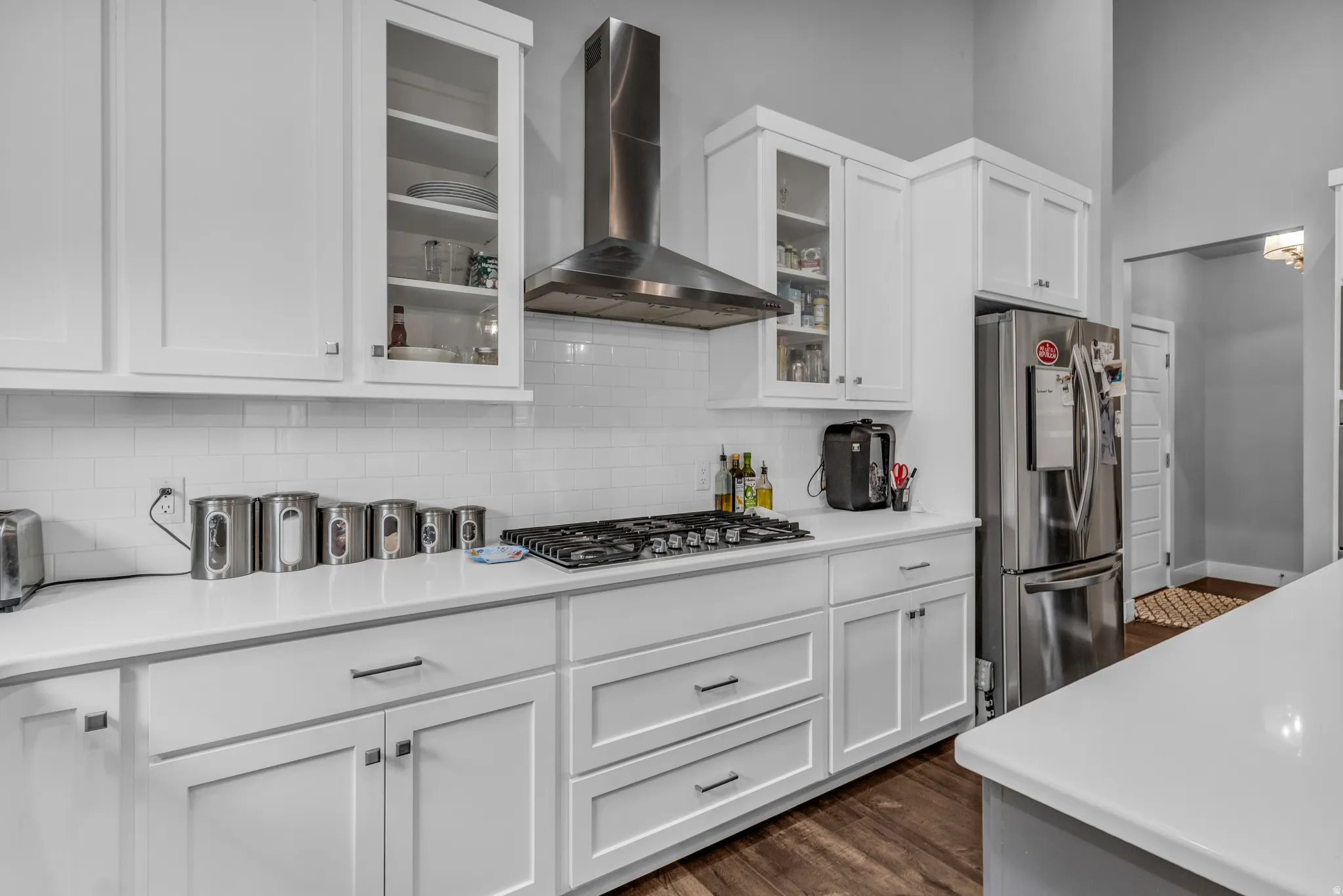 Kitchen featuring wall chimney exhaust hood, white cabinetry, stainless steel appliances, tasteful backsplash, and dark wood-style floors