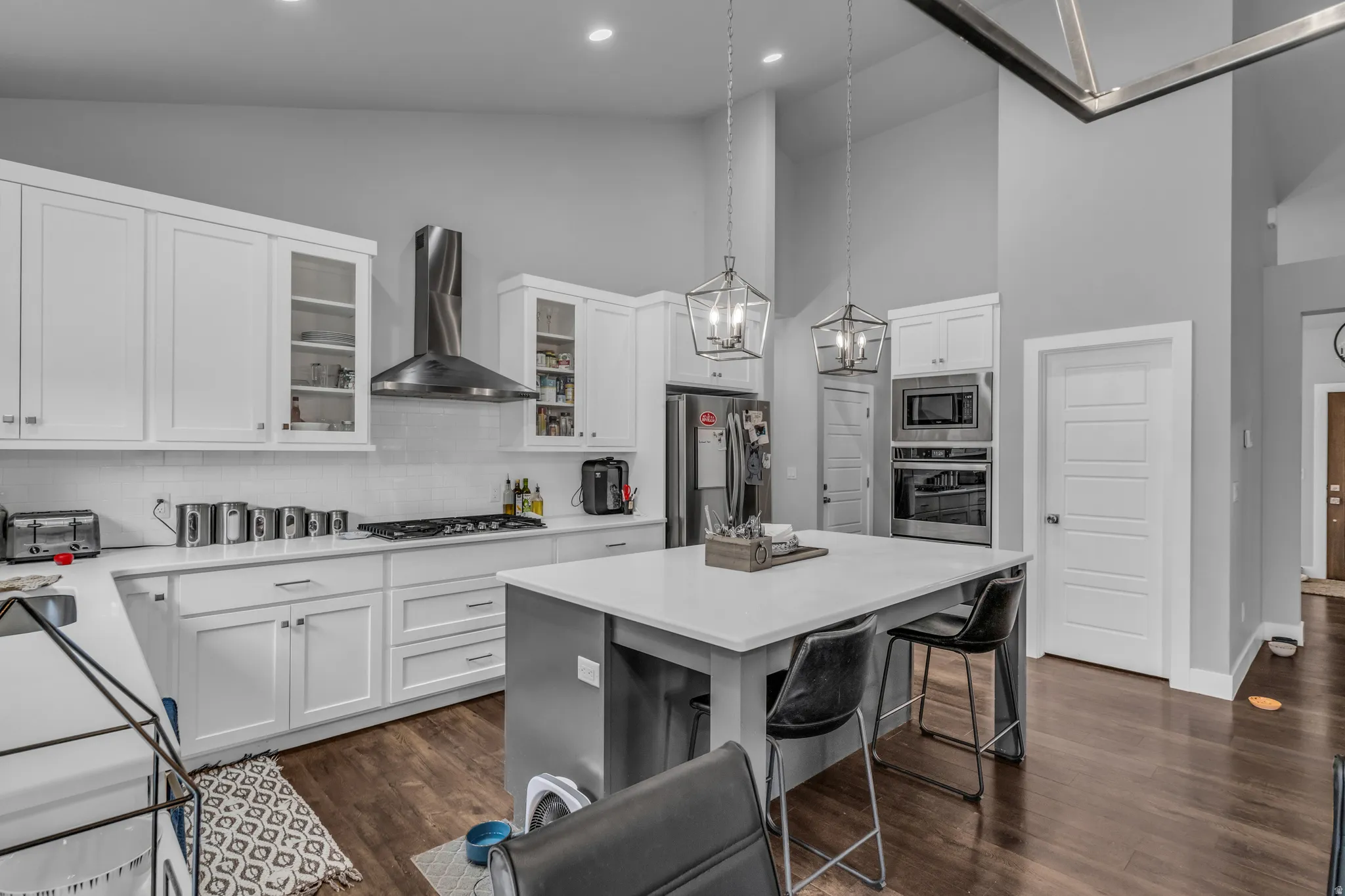 Kitchen featuring a kitchen bar, pendant lighting, high vaulted ceiling, glass insert cabinets, and dark wood finished floors