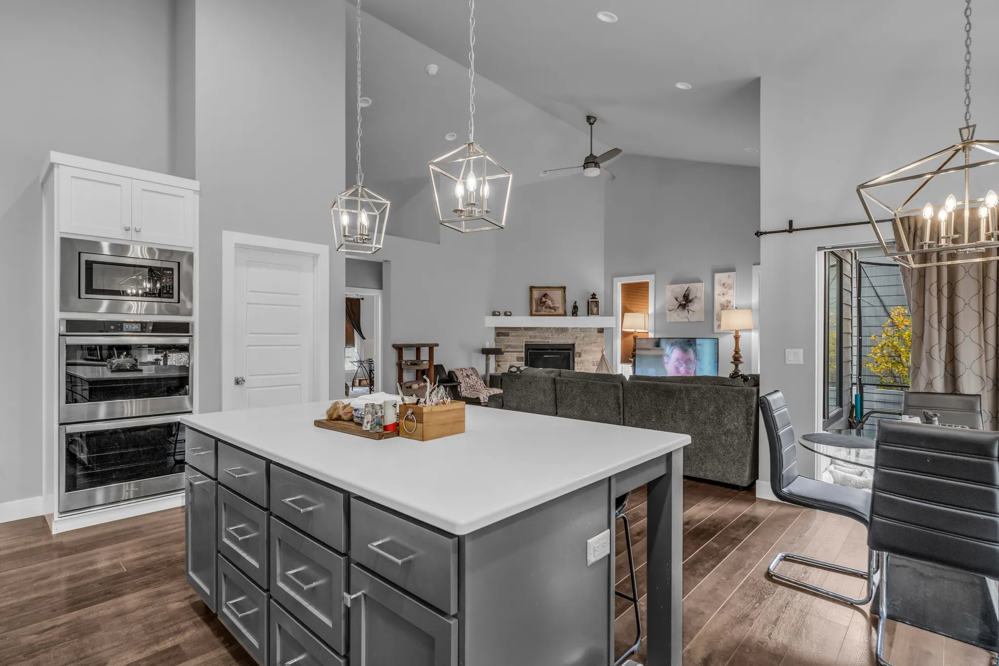 Kitchen featuring a chandelier, high vaulted ceiling, a stone fireplace, ceiling fan, and dark wood-style floors