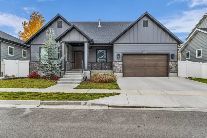 Craftsman-style home with stone siding, board and batten siding, driveway, a garage, and a gate