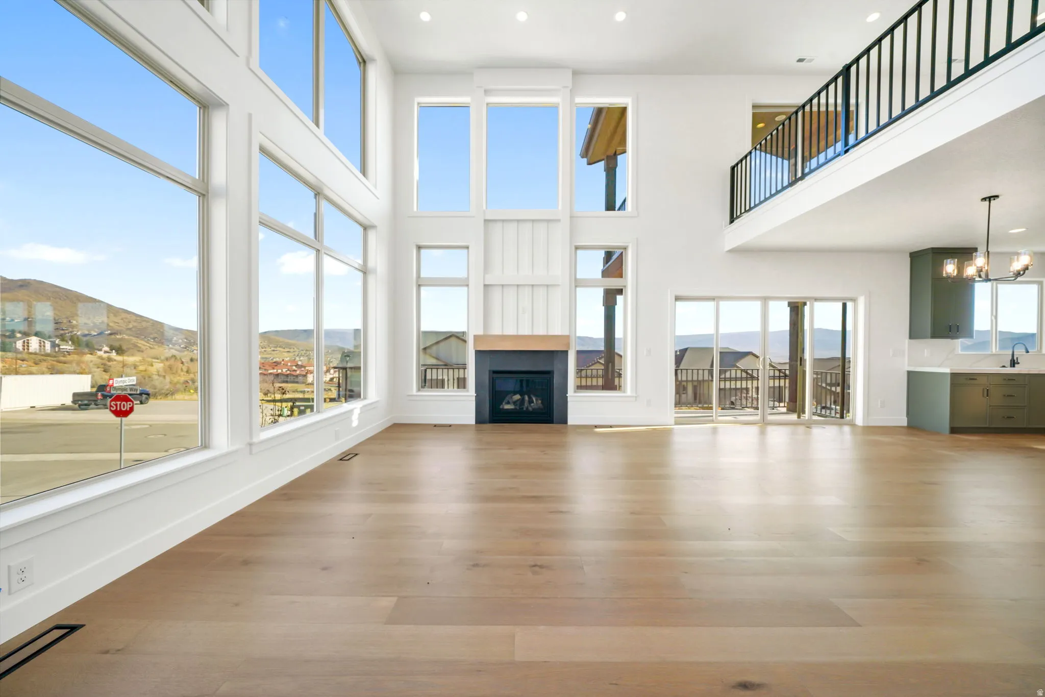 Unfurnished living room with a mountain view, a glass covered fireplace, light wood-style floors, recessed lighting, and a towering ceiling