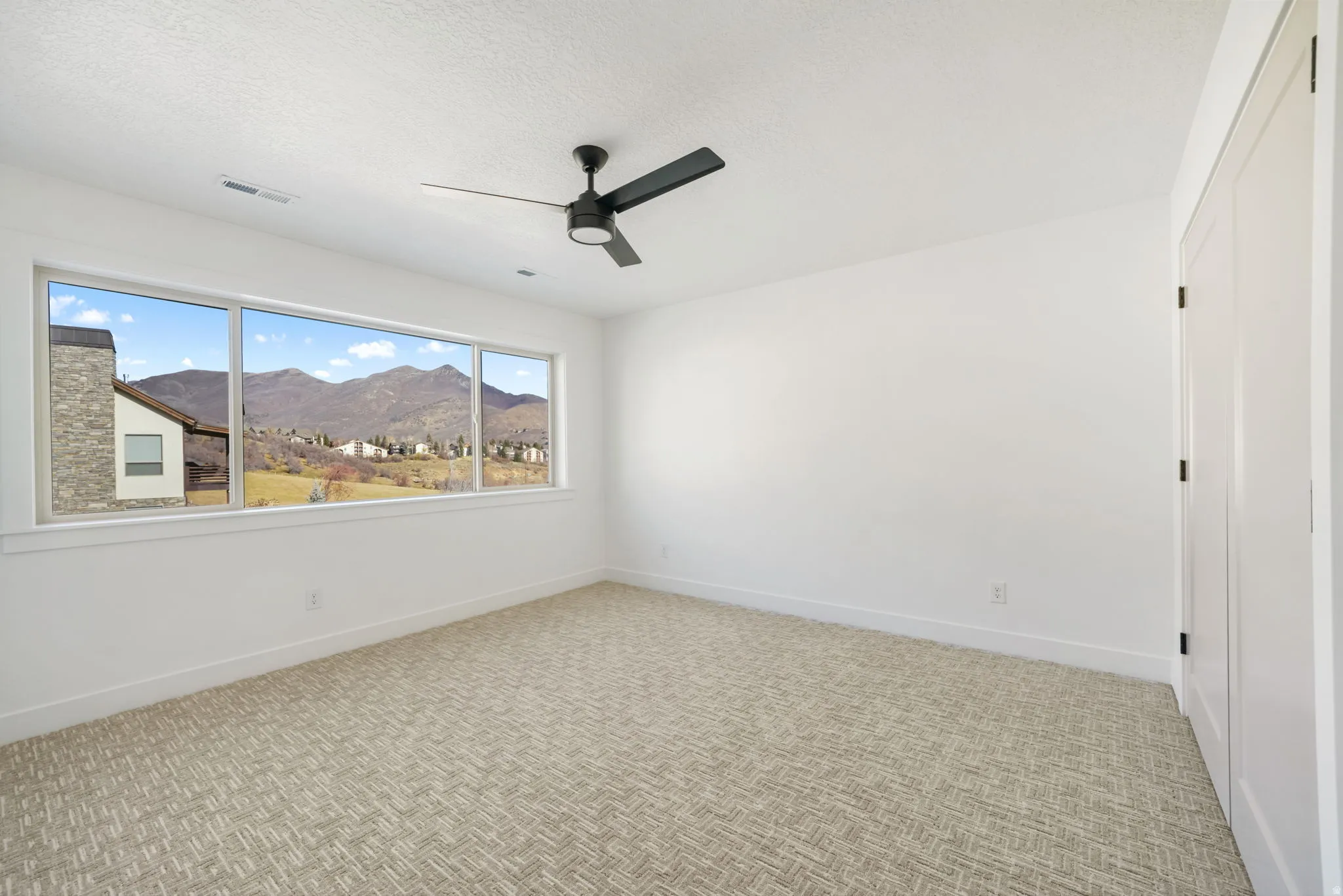 Unfurnished room featuring a mountain view, light carpet, a ceiling fan, and a textured ceiling