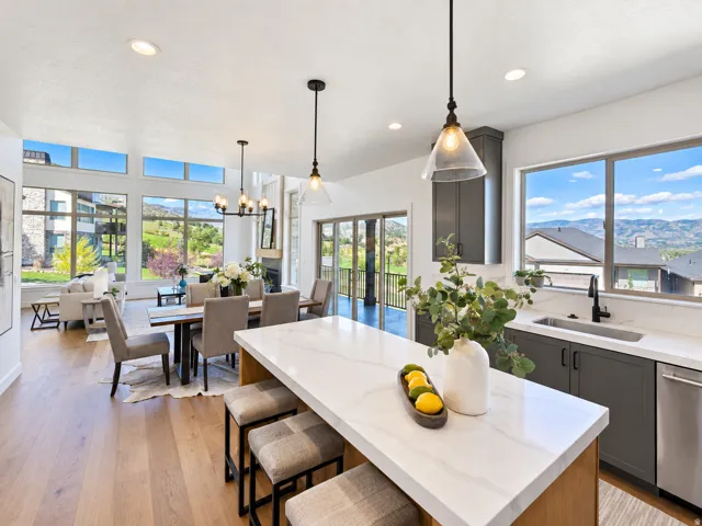 Open-concept living space with wood-finish flooring, a kitchen island with seating, dark grey cabinetry, and large windows