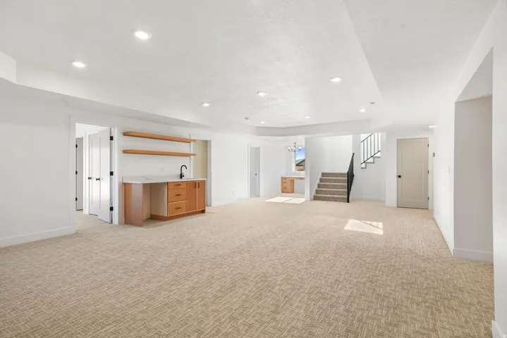 Unfurnished living room featuring light colored carpet, recessed lighting, stairs, bar with sink, and a tray ceiling