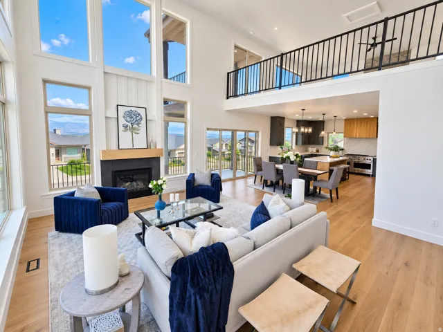 Vaulted ceiling great room featuring a fireplace with a wood mantel, expansive windows, open-concept kitchen, and a second-story interior balcony