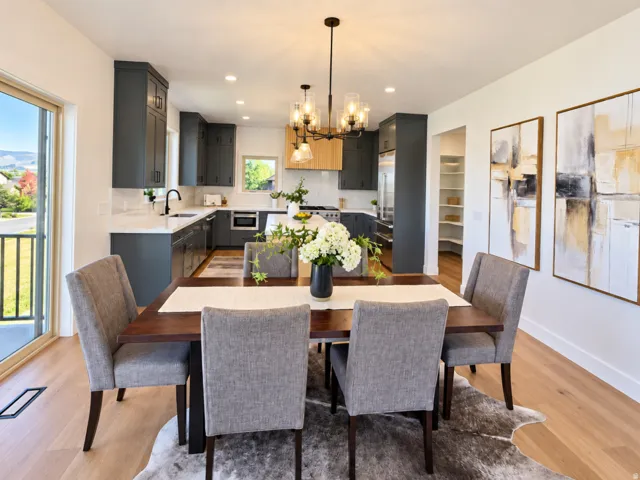 Open-concept living area with light wood-finish flooring, featuring a kitchen with dark cabinetry and light countertops, and a dining area with a contemporary chandelier