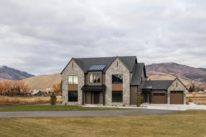 View of front of house with stone siding, a mountain view, a standing seam roof, driveway, and a front lawn