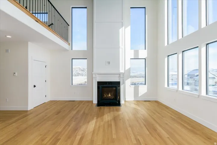 Unfurnished living room with light wood-type flooring, a high ceiling, and a high end fireplace