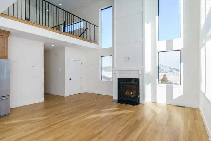 Unfurnished living room featuring a towering ceiling, light wood finished floors, and a fireplace with flush hearth