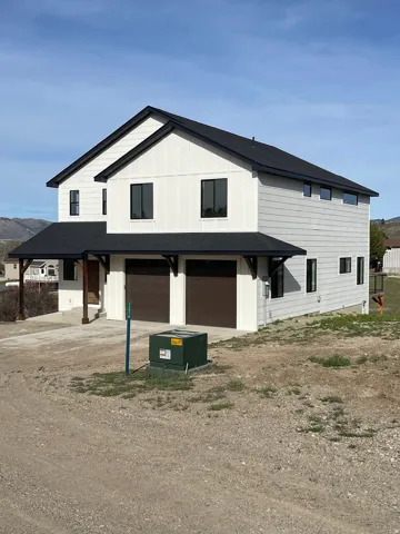 Modern farmhouse style home featuring a garage, board and batten siding, dirt driveway, and roof with shingles