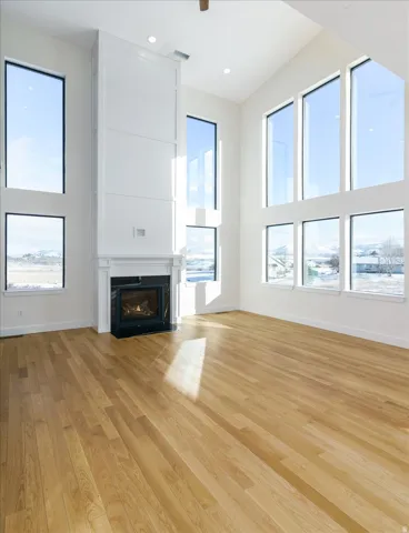 Unfurnished living room featuring a towering ceiling, light wood-style flooring, a fireplace with flush hearth, healthy amount of natural light, and recessed lighting