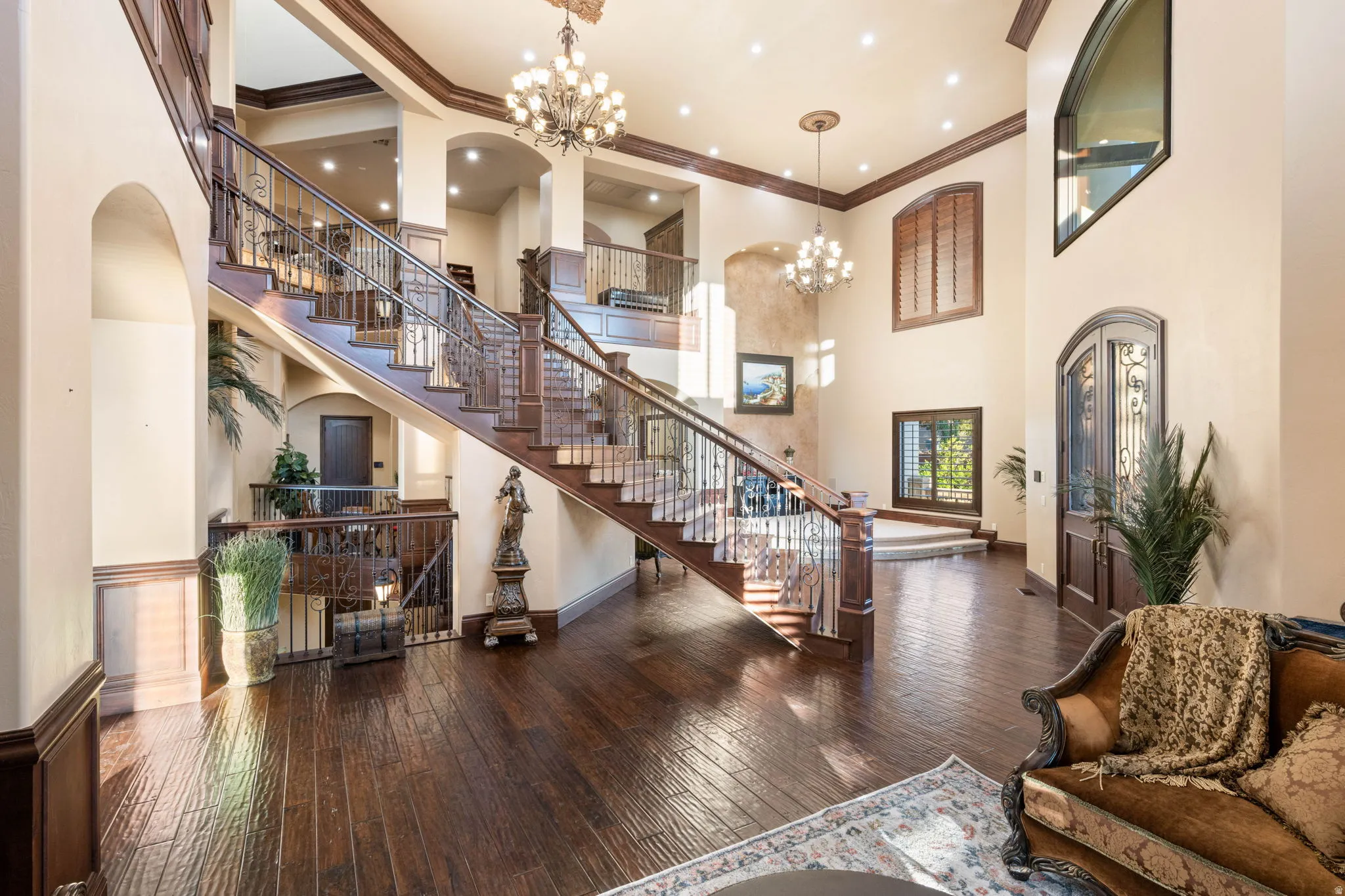 Living area featuring ornamental molding, arched walkways, dark wood-style flooring, a chandelier, and a high ceiling