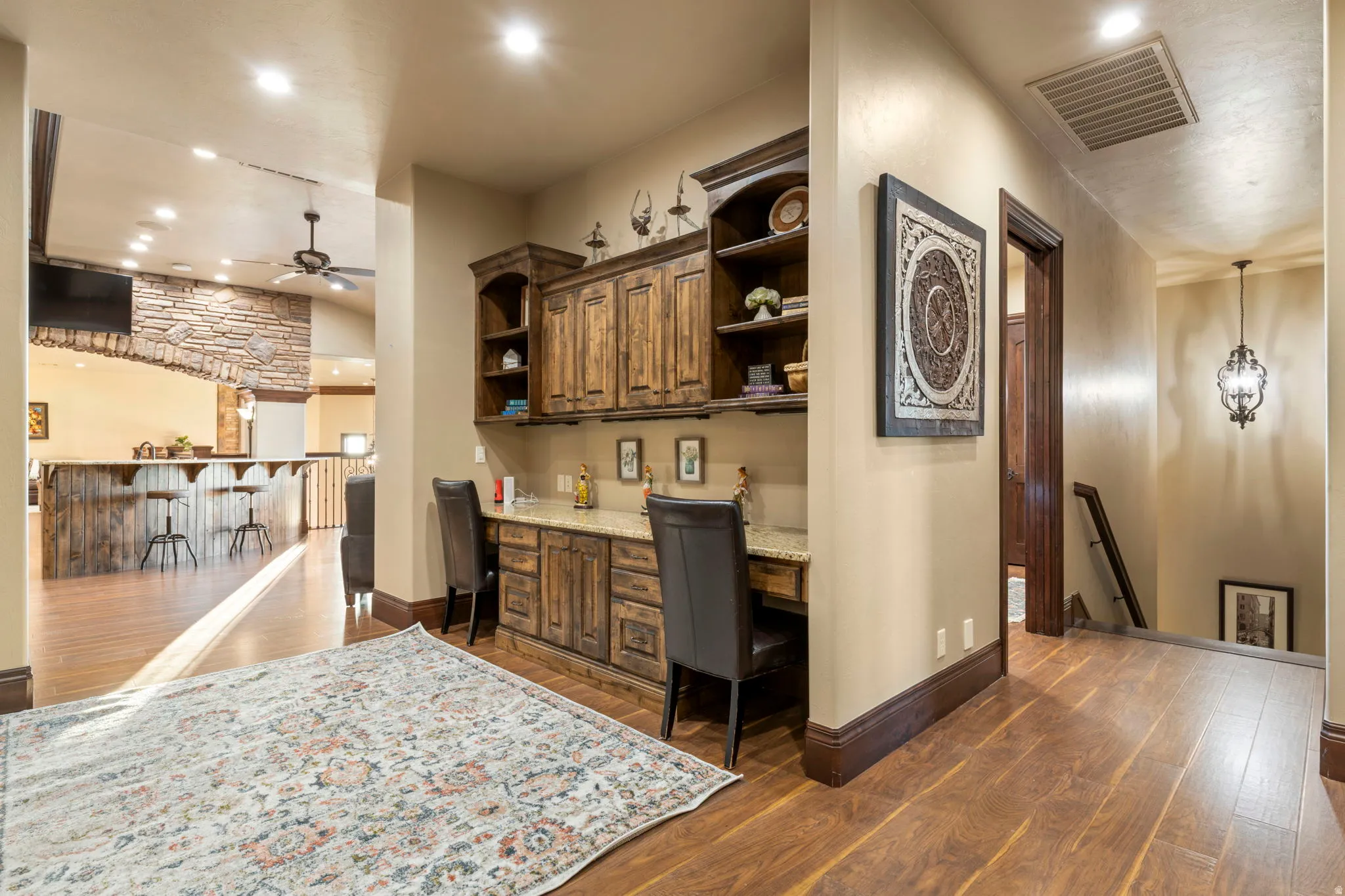 Bar area with built in study area, dark wood finished floors, open shelves, recessed lighting, and light stone counters