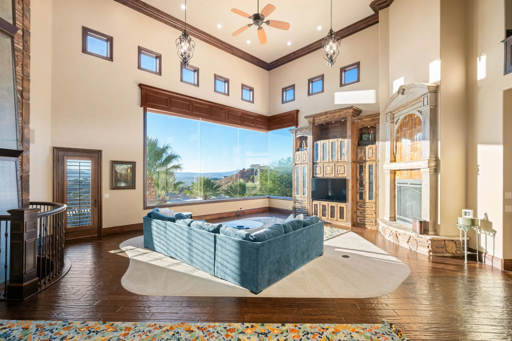 Living room featuring a high ceiling, a fireplace with raised hearth, crown molding, ceiling fan, and wood-type flooring
