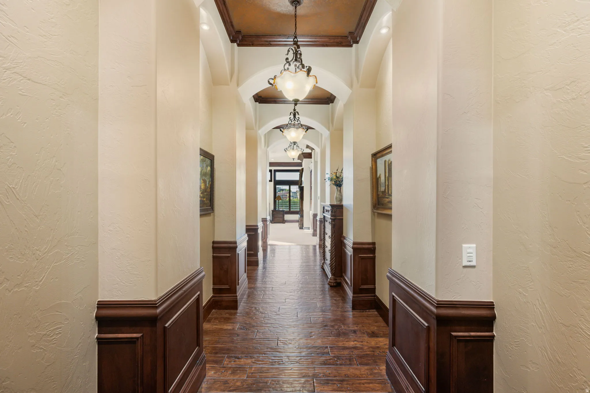 Hallway with a textured wall, arched walkways, crown molding, wainscoting, and dark wood-style flooring