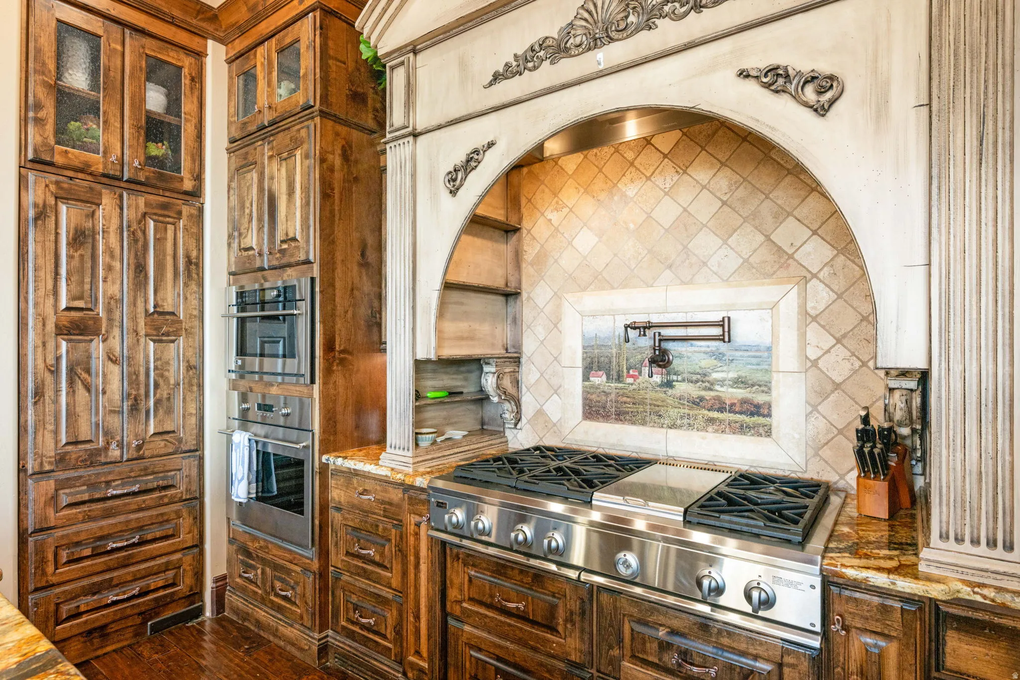 Kitchen featuring backsplash, light stone countertops, stainless steel gas stovetop, exhaust hood, and brown cabinets