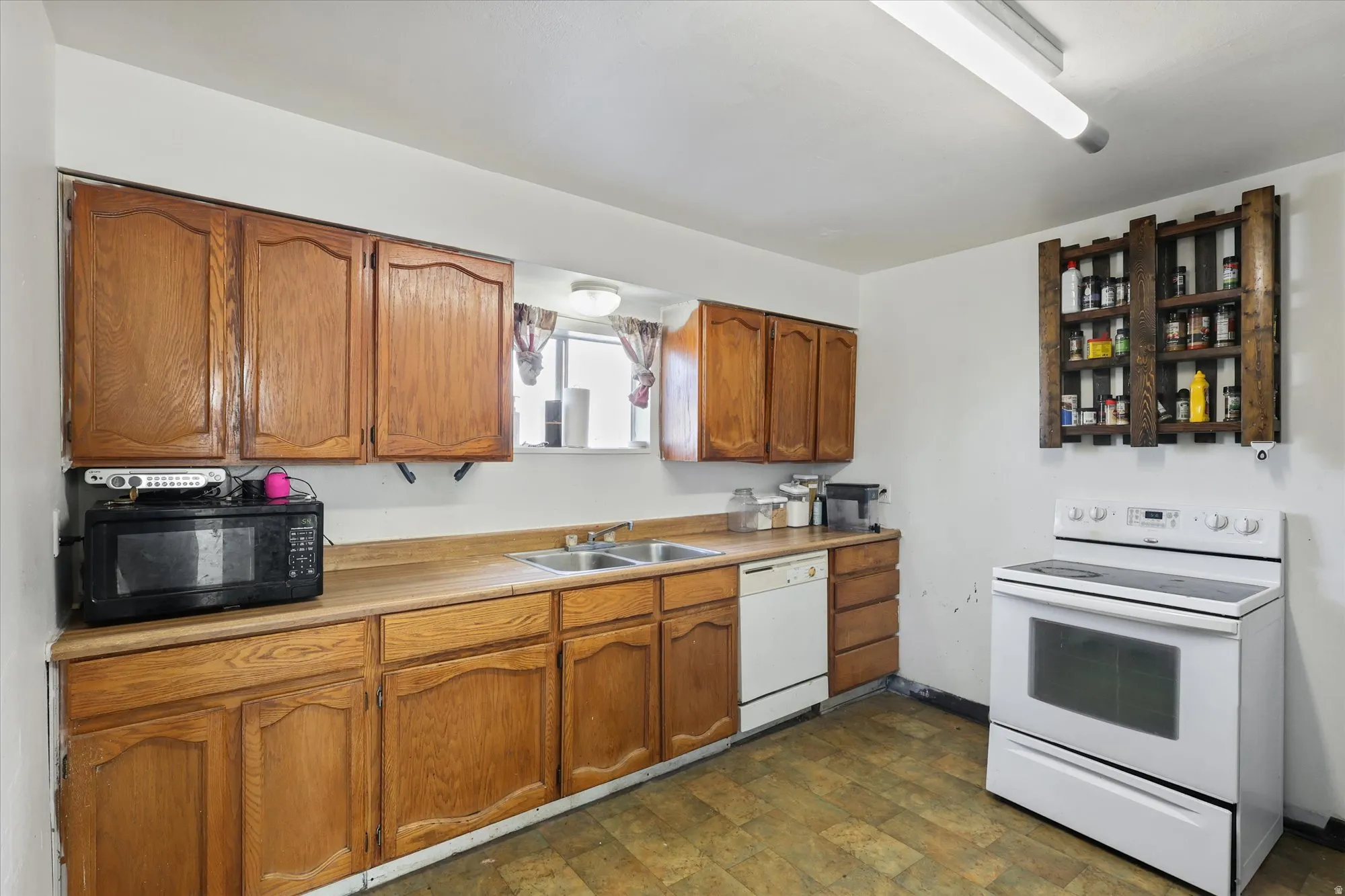 Kitchen featuring white appliances, brown cabinetry, light countertops, and stone finish flooring