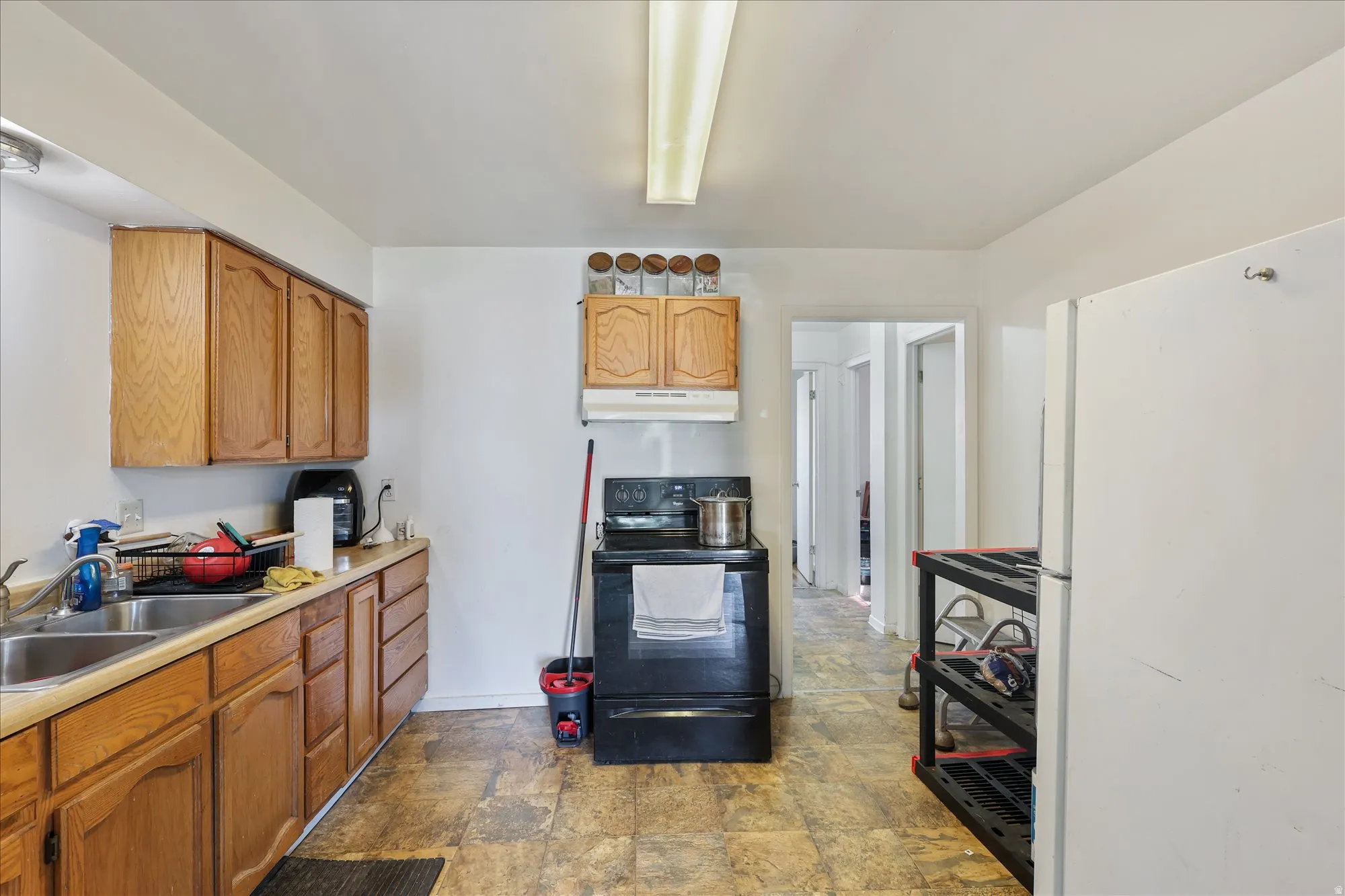 Kitchen with freestanding refrigerator, black range with electric cooktop, light countertops, stone finish floors, and brown cabinetry