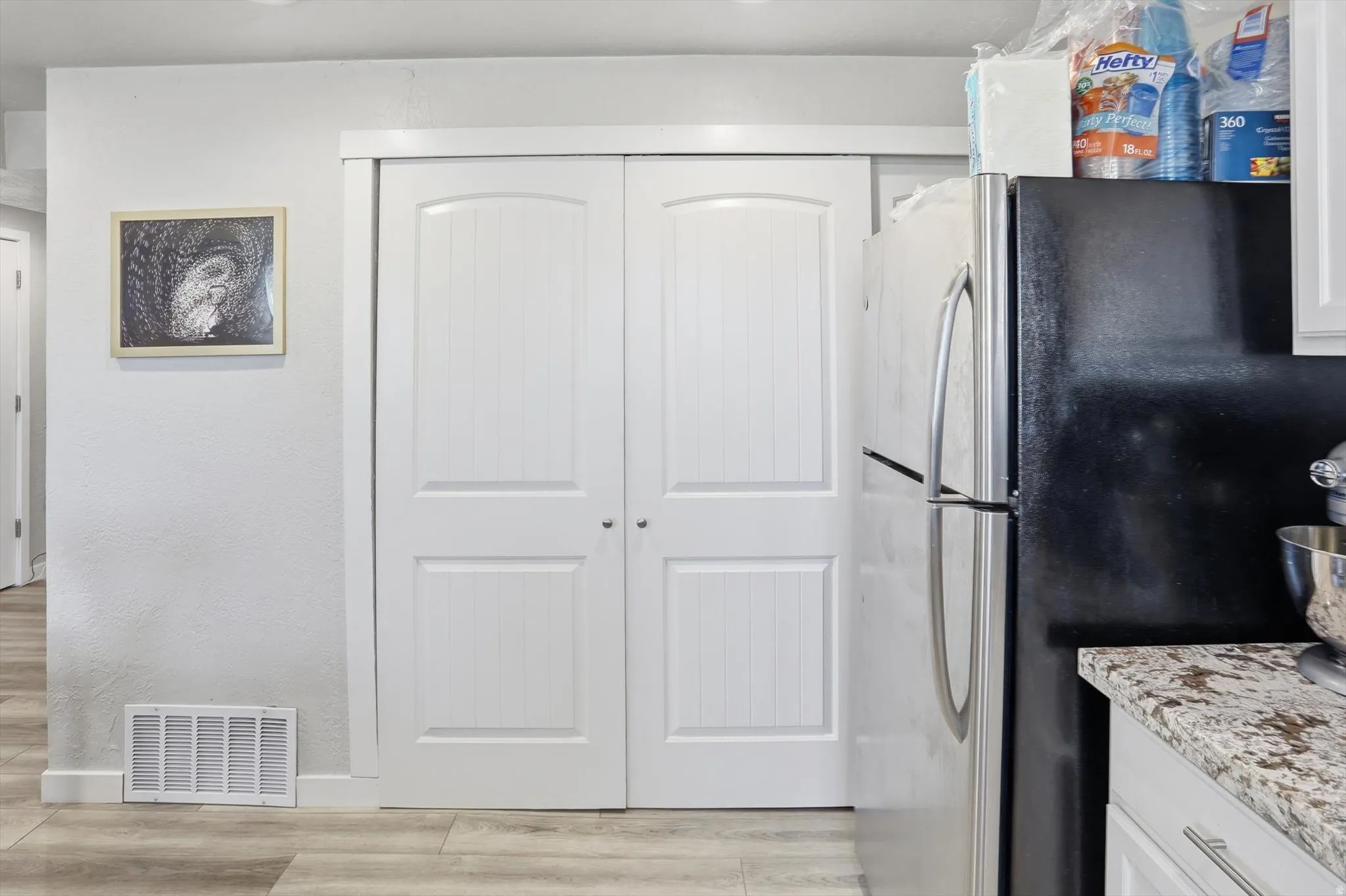 Kitchen featuring white cabinetry, freestanding refrigerator, light wood-type flooring, light stone countertops, and a textured wall