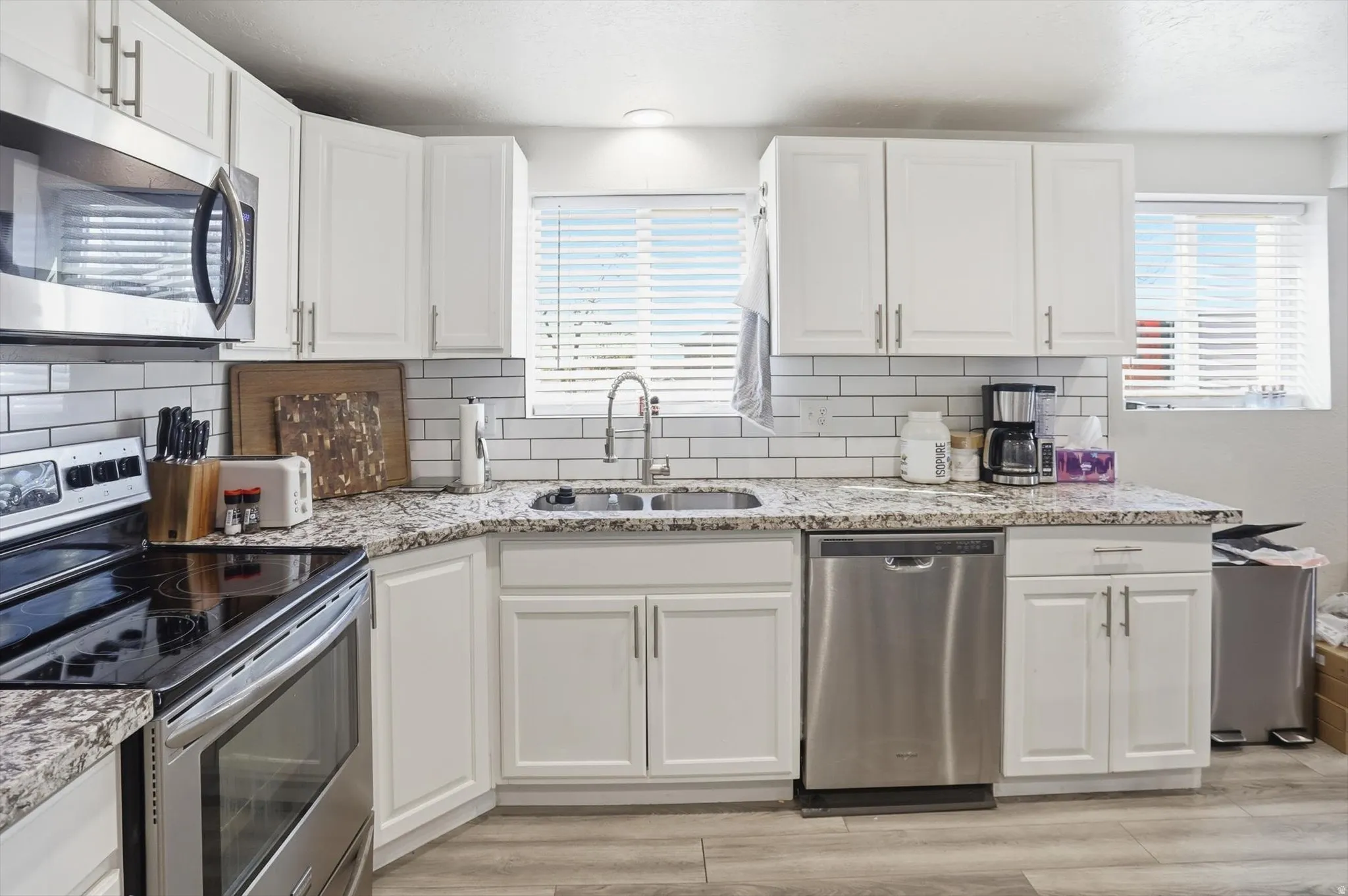Kitchen with appliances with stainless steel finishes, white cabinetry, backsplash, and light stone counters