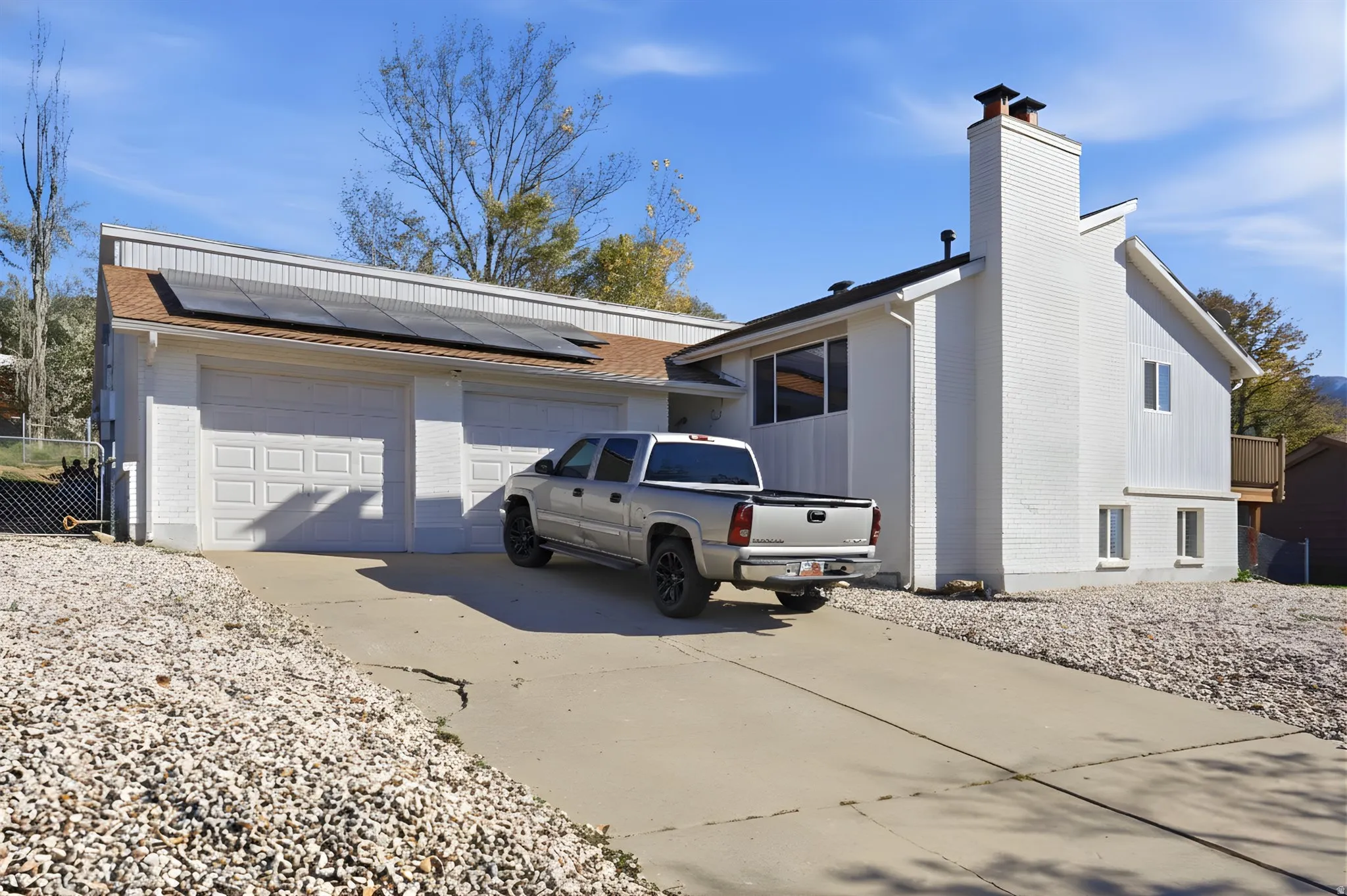 View of side of property featuring brick siding, driveway, a chimney, solar panels, and a garage