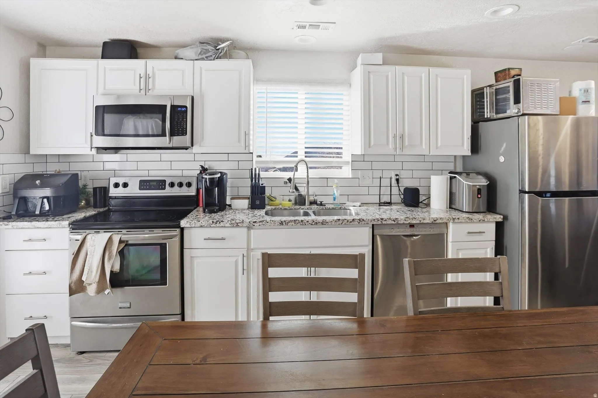 Kitchen with appliances with stainless steel finishes, white cabinets, light stone counters, decorative backsplash, and wood finished floors