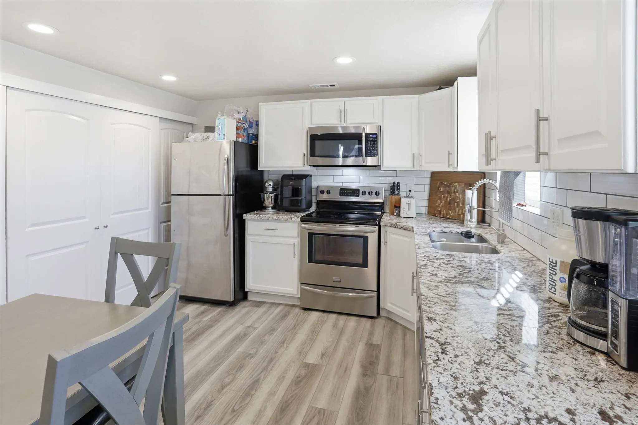 Kitchen with appliances with stainless steel finishes, light stone counters, tasteful backsplash, white cabinets, and light wood-style flooring