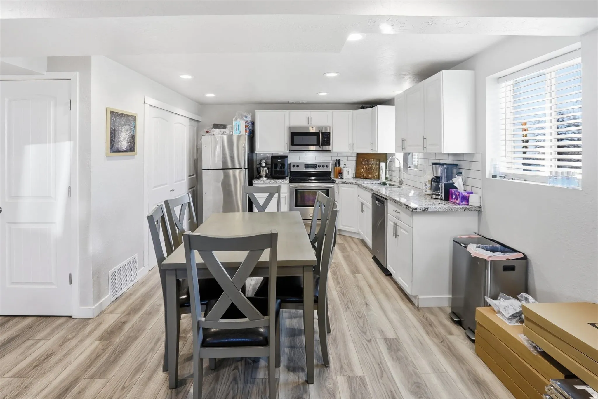 Kitchen with white cabinetry, light stone countertops, stainless steel appliances, backsplash, and light wood finished floors