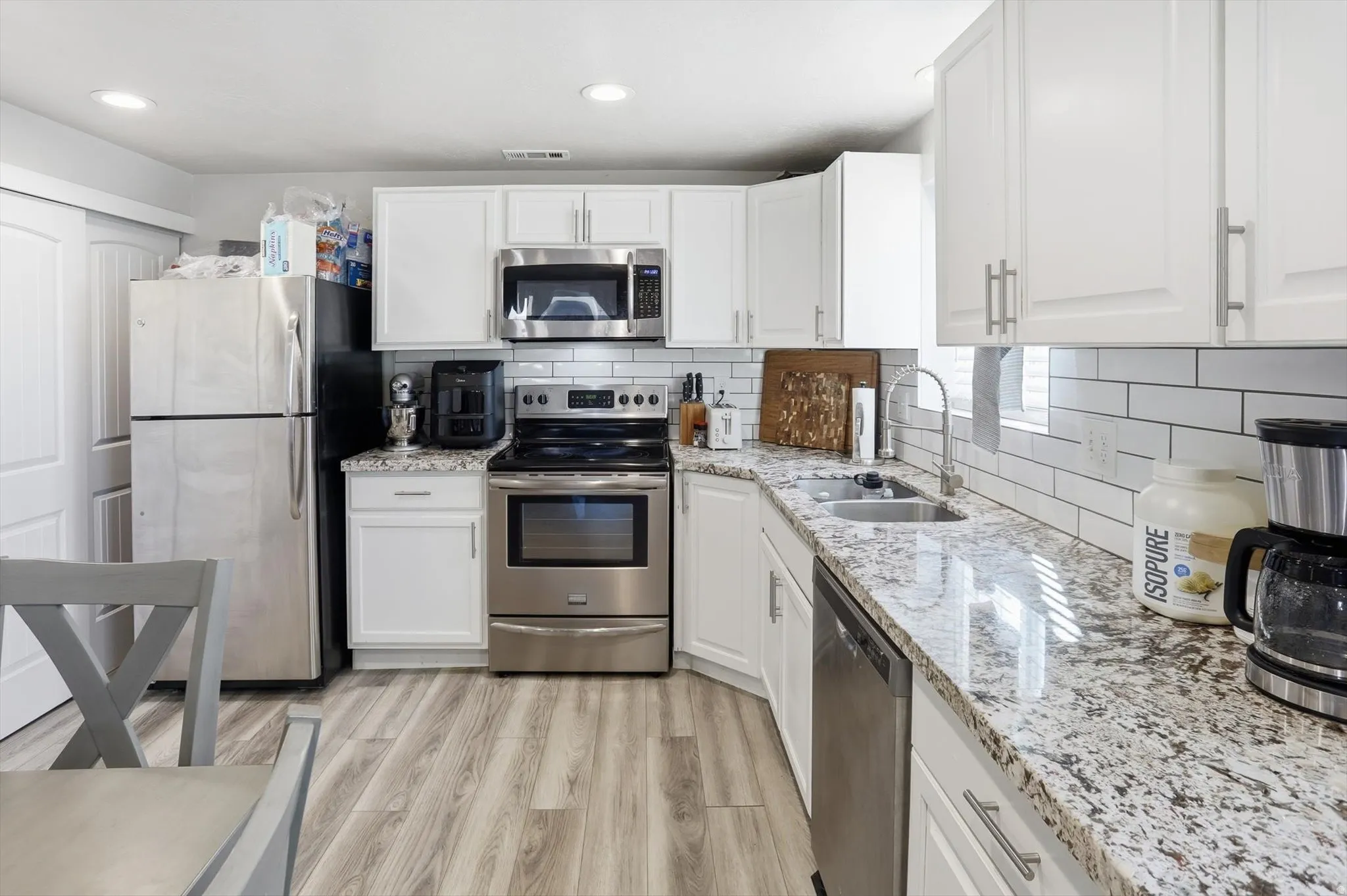 Kitchen featuring white cabinetry, stainless steel appliances, light stone counters, and recessed lighting