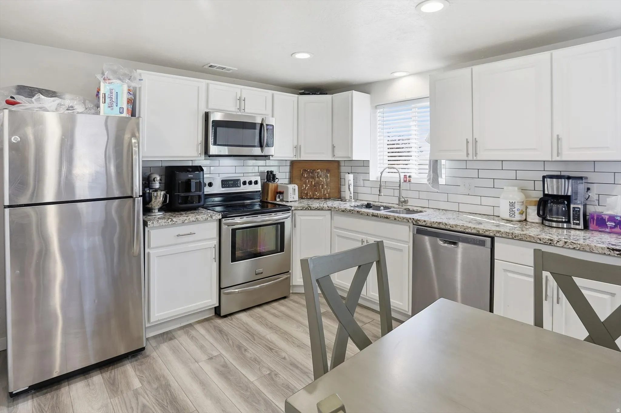 Kitchen with appliances with stainless steel finishes, white cabinetry, light stone countertops, tasteful backsplash, and light wood-type flooring