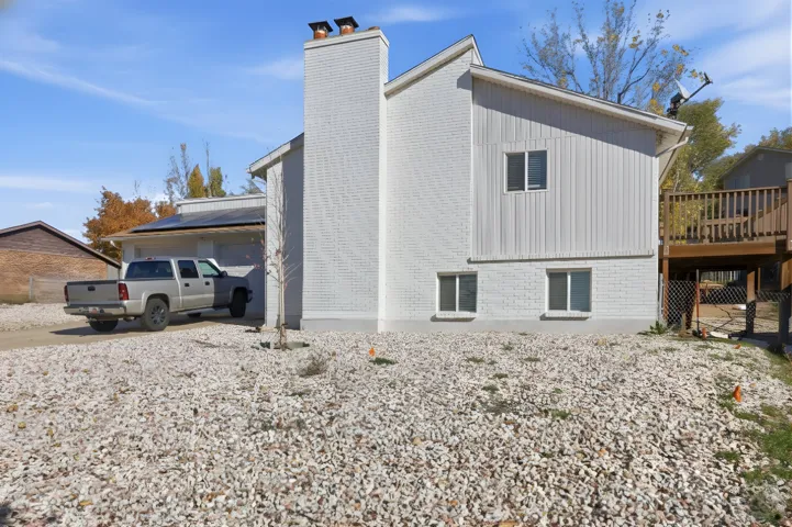 View of property exterior featuring a chimney, driveway, brick siding, and a deck