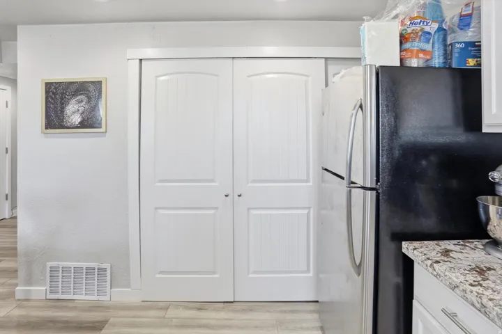 Kitchen featuring white cabinetry, freestanding refrigerator, light wood-type flooring, light stone countertops, and a textured wall
