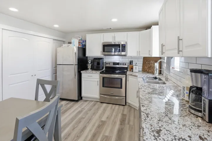 Kitchen with appliances with stainless steel finishes, light stone counters, tasteful backsplash, white cabinets, and light wood-style flooring