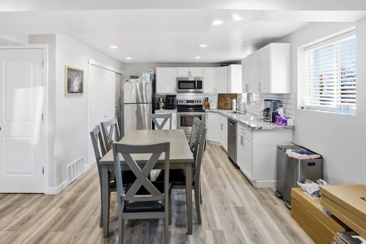 Kitchen with white cabinetry, light stone countertops, stainless steel appliances, backsplash, and light wood finished floors