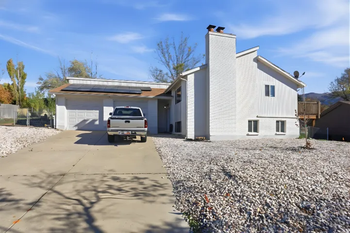 View of side of home featuring brick siding, a chimney, concrete driveway, solar panels, and an attached garage